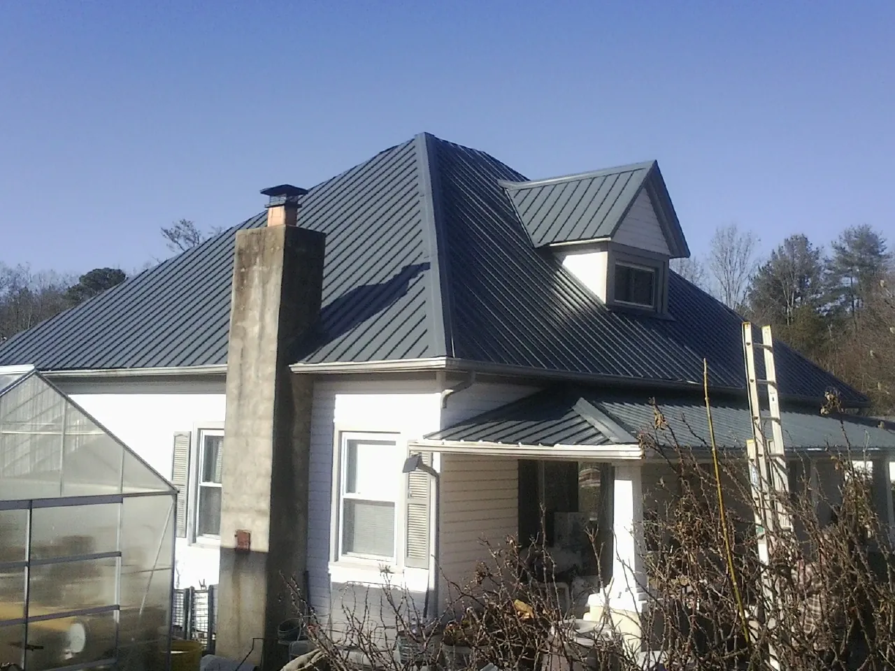 Dark blue standing seam metal roof on a white farmhouse with dormer — Slate & Tile Roof Repair by Roofing Brothers in Sagaponack