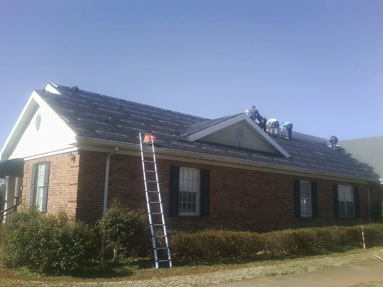 Crew tearing shingles off a brick ranch roof with a ladder set — Emergency Roof Repair work by our crew in Sagaponack