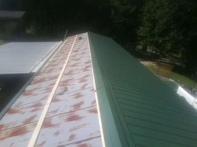 Old rusted panels beside newly installed green metal roofing — Wind Damage Roof Repair by Roofing Brothers in Sagaponack