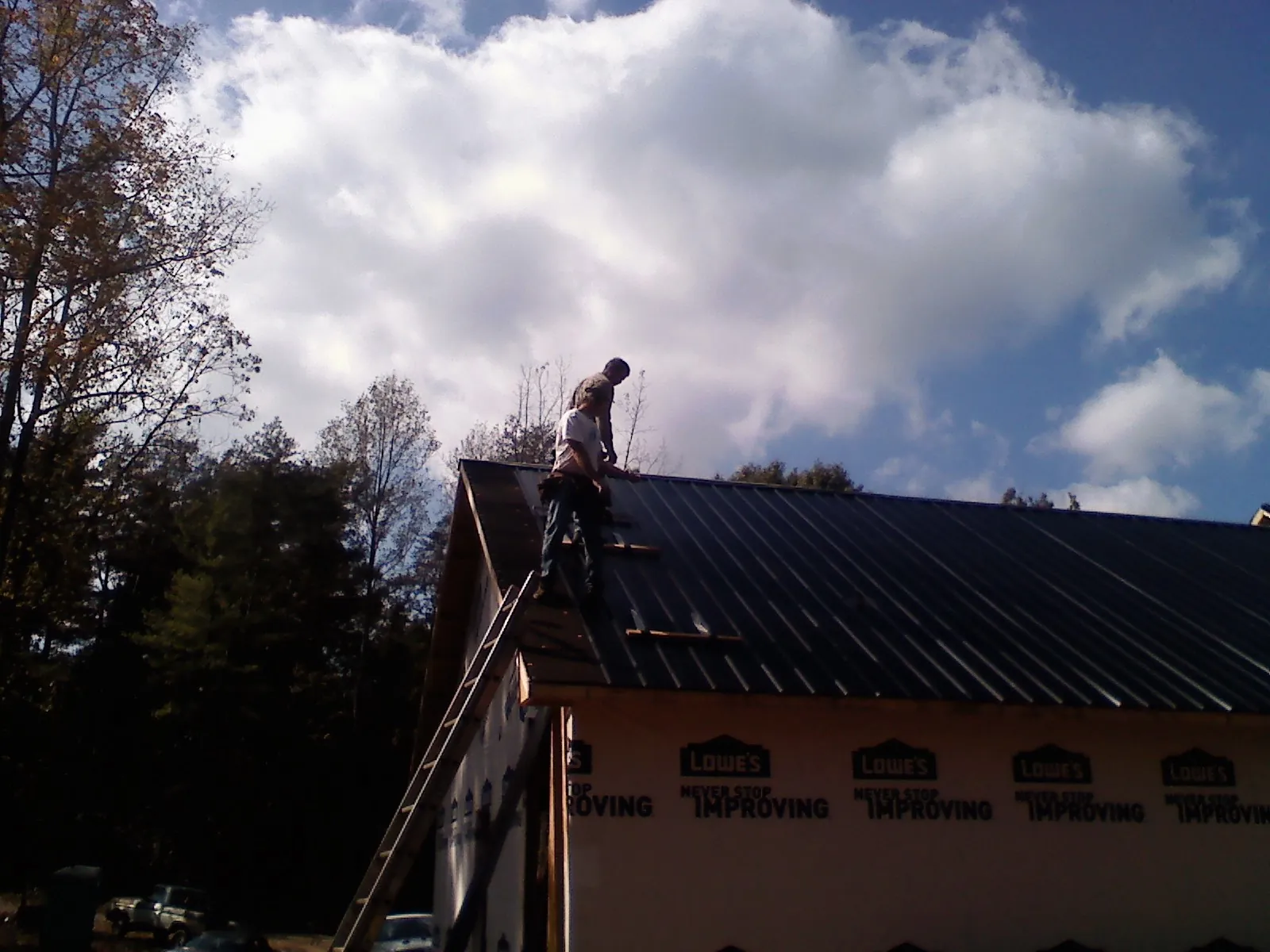 Roofer fastening dark metal panels high against a cloudy sky, from a Roof Inspection job in Sagaponack