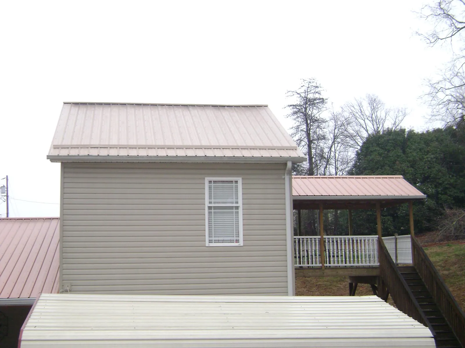 Tan metal roofs on a two story addition and attached porch, from a Roof Replacement job in Sagaponack